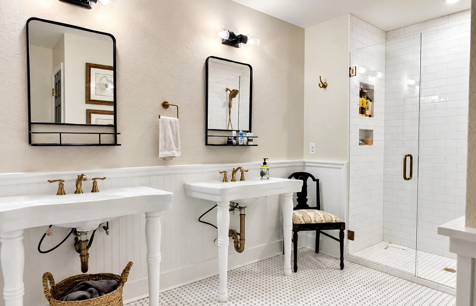 Bright bathroom with white console sinks, black-framed mirrors, beadboard walls, and a glass-enclosed subway-tile shower installed by Meza Tile and Stone